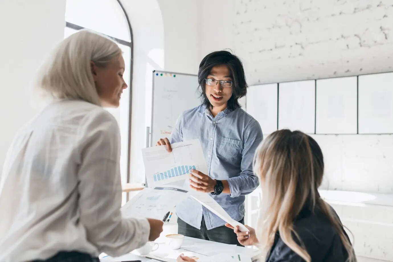 Guapo estudiante asiático explicando algo a sus compañeros de universidad mientras sostiene gráficos económicos.